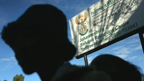 A silhouetted figure in a hat stands in line near the entrance of a government refugee centre in Johannesburg, South Africa - archive shot