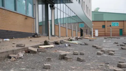 Bricks and rubble on the floor of a car park in front of a brick, glass and chrome building.