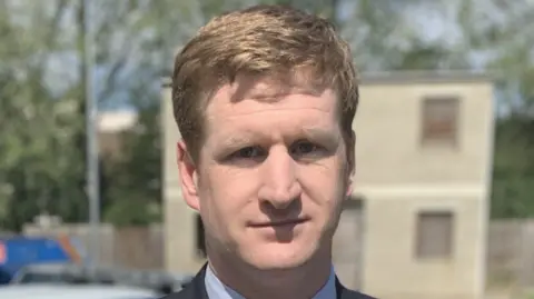 KENT POLICE AND CRIME COMMISSIONER Kent Police and Crime Commissioner Matthew Scott in front of a police car.