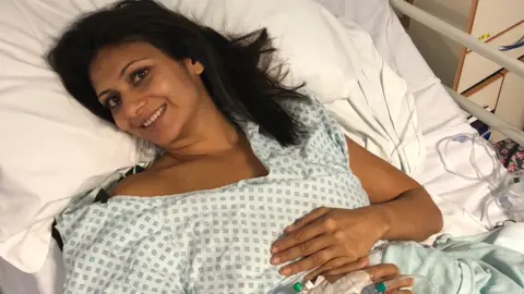 Anisha Patel Anisha on a hospital bed, smiling to camera