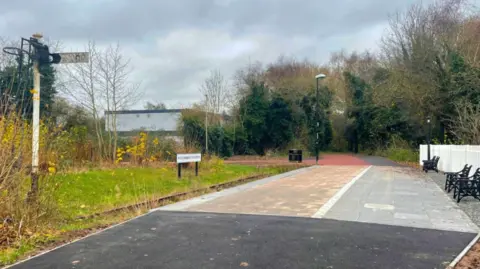 Leicester City Council A railway platform next to a disused overgrown track.  A signal post can be seen on the left of the image
