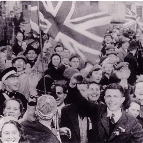 A crowd of people with smiling faces waving union flags