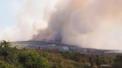 Simon Torr Orange flames beneath thick plumes of smoke over a field in Cornwall.