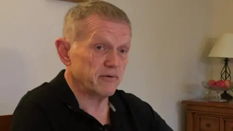 Richard Barker sitting at his dining room table looking over paperwork to do with his investment in Arndale House in Liverpool. 