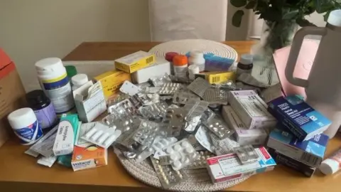 Evie Solomon A brown table covered in a variety of medication tubs, packets and tablet strips