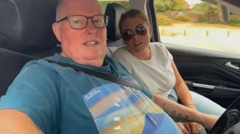 A man and a woman in a car looking into the camera