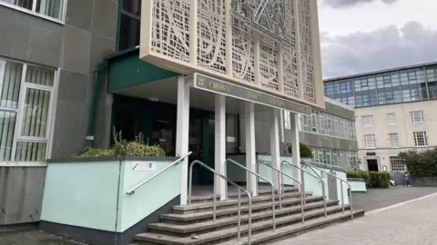 A picture taken from the left side of Plymouth Crown Court looking over to the entrance. It is a large entrance with steps and railings.