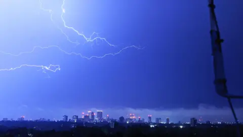ArniePie Blue-coloured lightning appears to strike sideways in the sky. The cityscape of Birmingham can be seen in the distance.