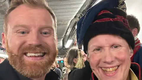 Boyd Rogers Boyd Rogers, on the left, has a ginger beard and is wearing a mic on his left cheek. He is standing beside Matt Lucas, who is dressed in character as Thenardier. He is wearing a blue floppy hat with a gold tassel. He also has stage make up on - including dirt smudged on his face and yellow staining on his teeth. The photo is cropped from the face up.