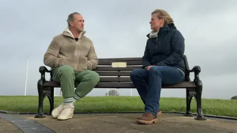 Paul Maxwell sits with BBC Spotlight presenter Victoria Graham on a bench on Plymouth Hoe