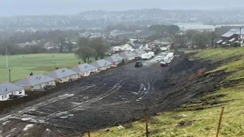 Houses to the left and a field to the right with mud that has been dug up in the centre of the picture