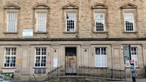 The Post Office branch in Kendal is a multi-storey white stone building with large white windows. The words: "Post Office" are engraved into the stone above the door.