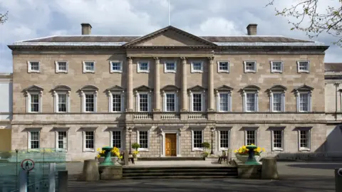 Getty Images Government Buildings on Kildare Street in Dublin 
Large brick building with large flowerpots either side of entrance with yellow flowers