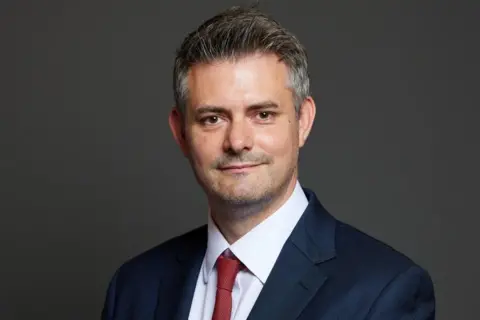 UK Parliament A man in a navy suit and a red tie.