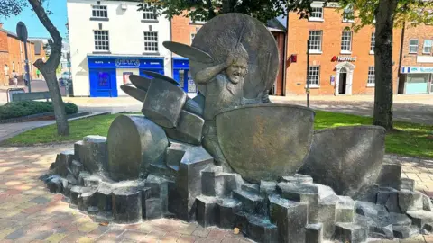 BBC The John Bonham Statue in Redditch town centre - a large sculpture of a man playing drums on a bed of rocks.