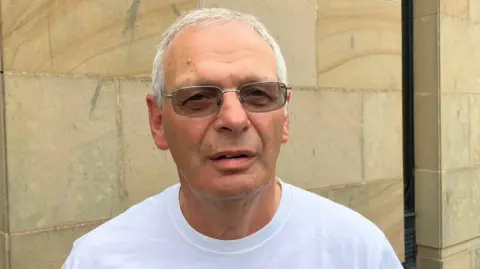 Steve Jones/BBC Neil Sevitt, who has short grey hair and dark-coloured tinted glasses. He has a neutral expression in the photo.