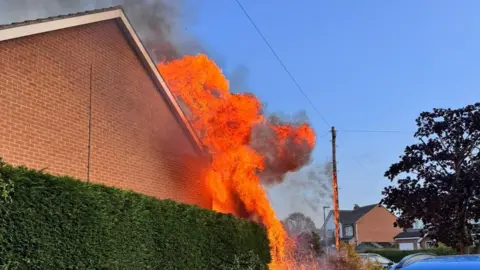 Julie Ball Flames licking the side of a house.