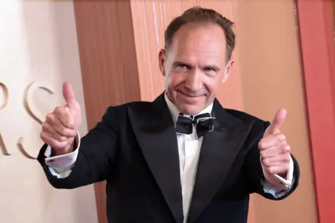 DAVID SWANSON/EPA-EFE/REX/Shutterstock Ralph Fiennes on the red carpet. He is smiling and is holding both thumbs up.