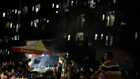 Xiqing Wang/BBC A man sells food in front of a block where workers live 