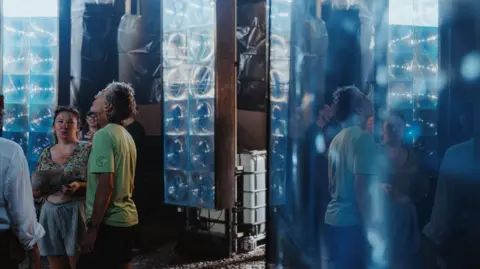 People walking amongst three tall panels of light at the light display at Jacob Wells Baths.