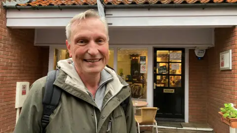 Simon Spark/BBC Dieter Krapp wearing a green jacket with a black bag on his back, smiling at the camera