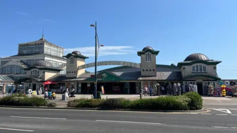 The front of the Wellington Pier on a sunny day with blue skies above, with the Winter Gardens building in the background.
