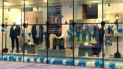 Kelly McCormack/BBC Store window showing Ipswich town flag and blue and white balloons