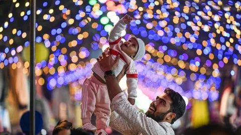 Getty Images A man lifts his child to see Diwali lights set up at Janpath Market in New Delhi