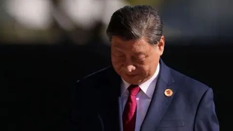 Getty Images Xi Jinping in a navy suit and red tie looks down at the ground in a photo taken at the G20 Summit 2024 n November 18, 2024 in Rio de Janeiro, Brazil. 