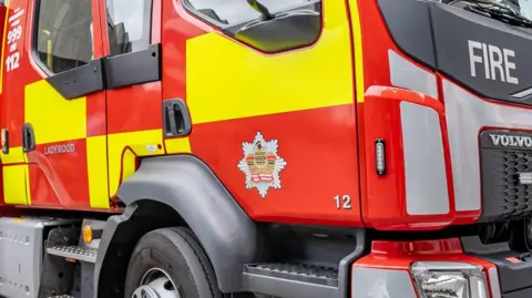 The side of a red fire engine, showing the door, wheel and the red and yellow markings.