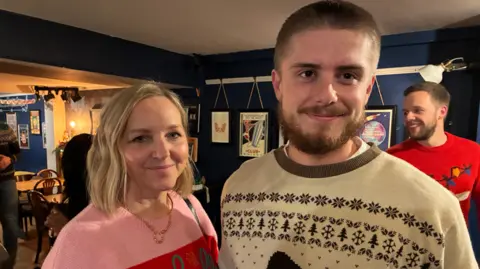 Woman in pink jumper and man in cream jumper in a pub setting 