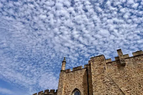 bbc weather watchers / Wynd-y-Miller The blue sky is tightly packed with rows of dots of clouds. In the foreground, are the turrets of a grand, brown stone building. The top of an arched window can just be made out.