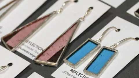Manchester City Council Different coloured and shaped glass dangly earrings displayed on a board.