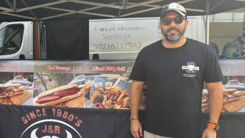 Three men smiling at the camera, stood in front of their food stall.