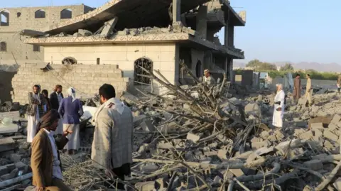 Men stand amid rubble in front of a damaged building in Saada