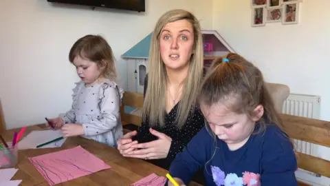 BBC/Nathan Turvey Lynsey Rogers (centre) with her daughters Daisy (right) and Bella (left) sitting at a table drawing pictures.