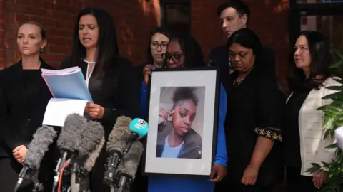 PA Media Hannah's mother, Abimbola Duyile, holds a picture of her daughter as solicitor Michelle Victor reads aloud a statement