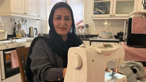 Khadija is sitting at her kitchen table with her sewing machine.