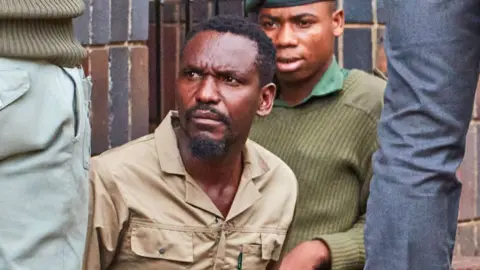 AFP Journalist Blessed Mhlanga in a khaki shirt frowns as he is surrounded by police outside court in Harare.