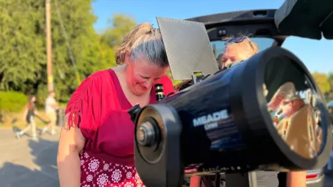 A woman is looking into a large telescope
