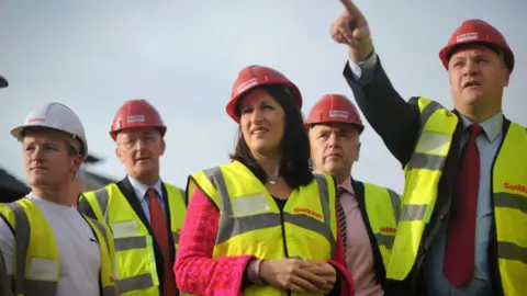 Getty Images Rachel Reeves and Ed Balls, pictured in 2012 visiting a social housing project with other Labour frontbench colleagues, wearing yellow high-vis jackets and red hard hats