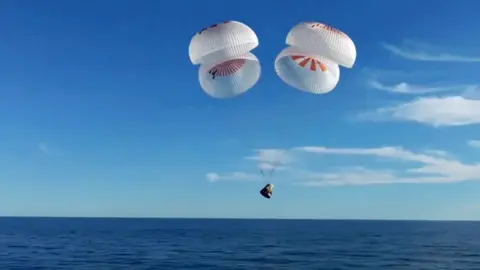 A space capsule plunging into water as the astronauts descended over the Atalantic off the coast of Florida against a blue sky on 18 March