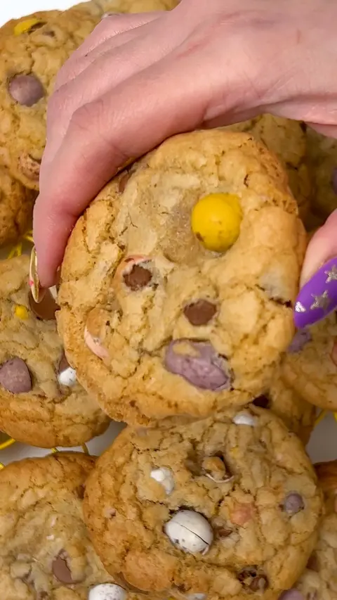 A woman's hand with colourful nails holds a cookie full of mini eggs
