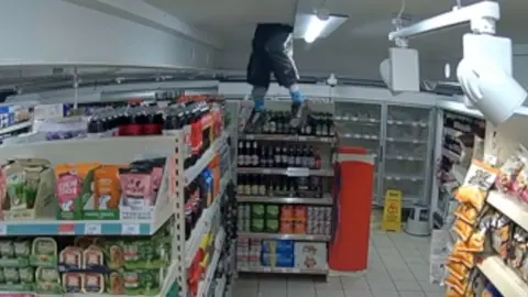 A CCTV still showing the burglar climb through the shop's ceiling