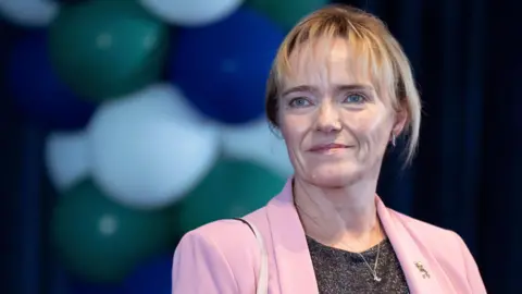 Sandie Peggie wearing a pink blazer over a black top staring slightly off camera.