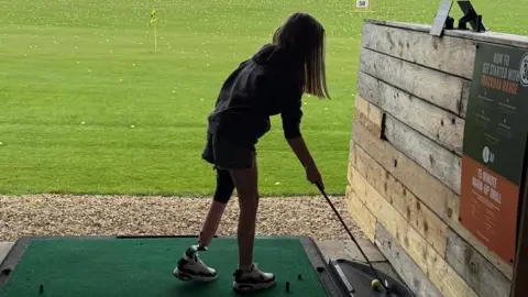 Family handout Rear view as Natalia prepares to swing a golf club at a range. She's wearing a hooded top and shorts with her prosthetic leg.