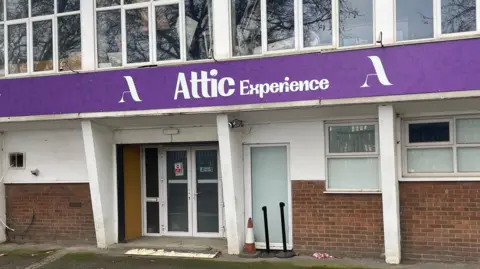 Building frontage with a purple sign with the words "Attic Experience"