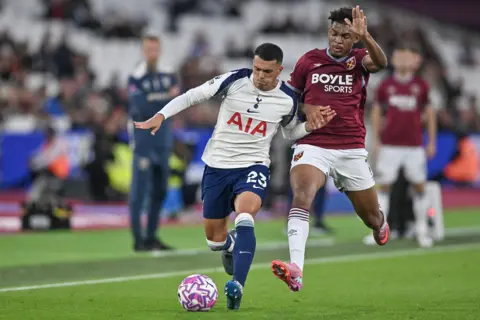 Getty Images Pedro Porro, in white kit, and Luis Guilherme, in claret, battle for a purple and white ball