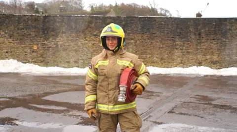 CDDFRS Mya Malthouse is standing holding a firehose under her arm. She's 20 years old and is wearing a firefighter's uniform.