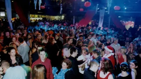 University of Sunderland A huge crowd of students in Halloween costumes dancing. Spider web decorations pumpkins are hanging from the ceiling.